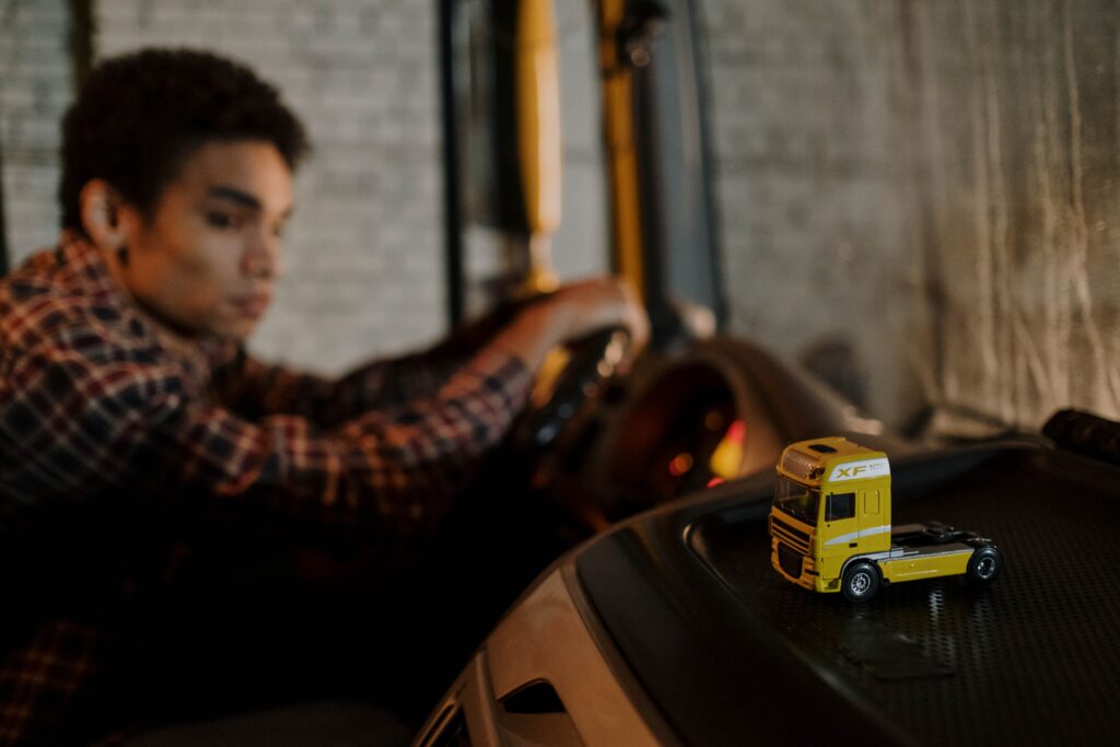 A driver in a truck cab with a focus on a miniature yellow truck toy, creating a blurred background.